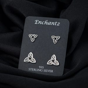 May include: A set of four sterling silver earrings featuring a Celtic knot design. The earrings are displayed on a black card with the brand name "Enchantz" and the text "925 Sterling Silver".