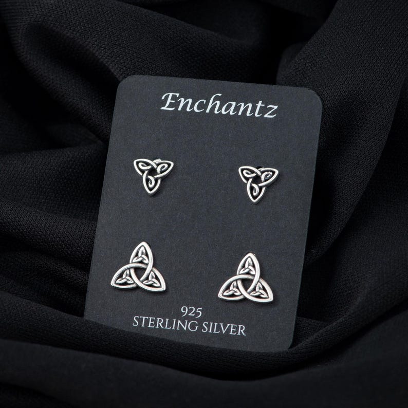 May include: A set of four sterling silver earrings featuring a Celtic knot design. The earrings are displayed on a black card with the brand name "Enchantz" and the text "925 Sterling Silver".