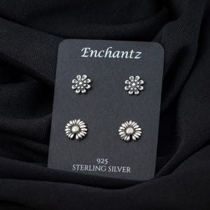 May include: Four silver daisy flower stud earrings on a black card with the text "Enchantz 925 Sterling Silver".