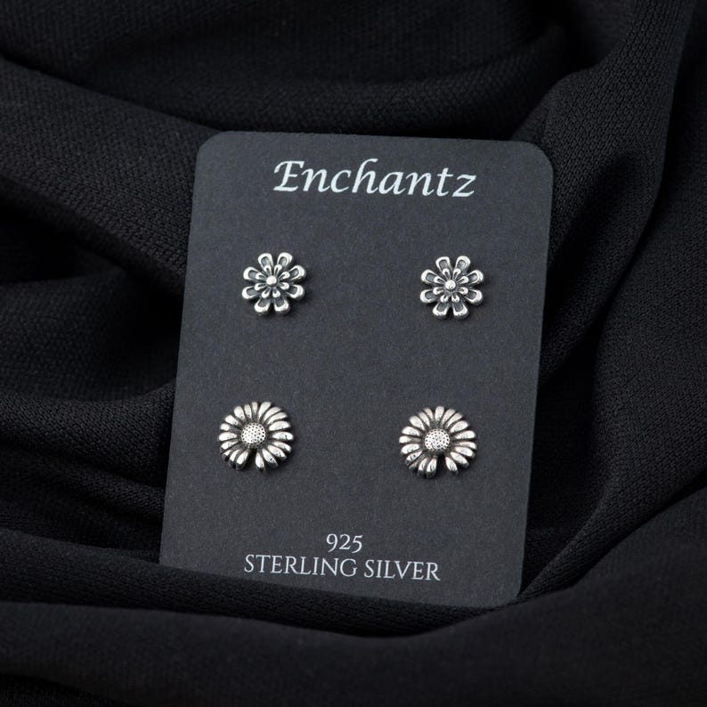 May include: Four silver daisy flower stud earrings on a black card with the text "Enchantz 925 Sterling Silver".