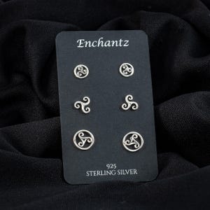 May include: A black card displays six sterling silver stud earrings with Celtic knot designs. The card reads "Enchantz" at the top and "925 Sterling Silver" at the bottom. The earrings are arranged in two rows of three.