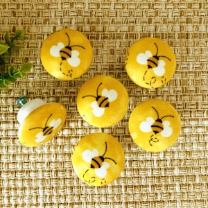 May include: Six yellow ceramic drawer knobs with a white bee design. The bees have black stripes and are flying with their wings spread.