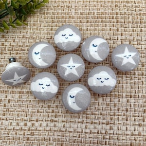 May include: Ten gray ceramic drawer knobs with white designs of a crescent moon, a star, and a cloud. Each design has a sleeping face.