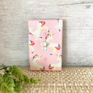 May include: A pink light switch cover with a white light switch and a pattern of white unicorns with rainbow manes and tails.