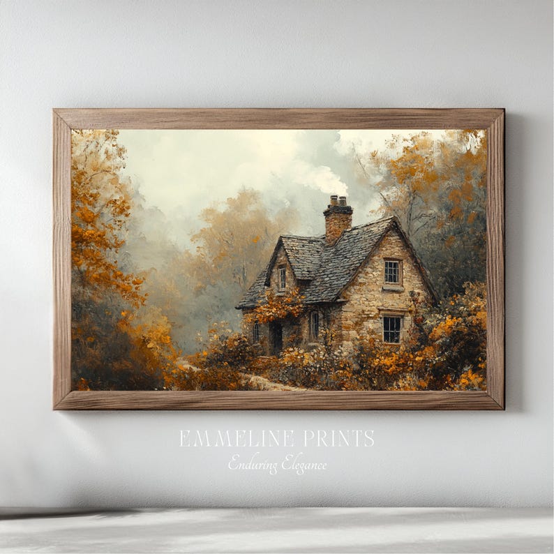 May include: A framed print of a quaint stone cottage nestled among trees with autumn foliage. The artwork features a muted color palette of browns, oranges, and greens, with the text "EMMELINE PRINTS Enduring Elegance" at the bottom.