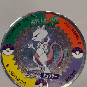 May include: Circular collectible featuring a purple and white Mewtwo character from the Pokémon franchise. The disc has a holographic finish and includes Japanese text and various colored segments with numbers and symbols.