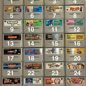 May include: A collection of twenty-eight grey Super Famicom video game cartridges arranged in a grid, each featuring a unique colourful label with Japanese text and character illustrations, numbered one through twenty-eight with the text Choose Any 10.