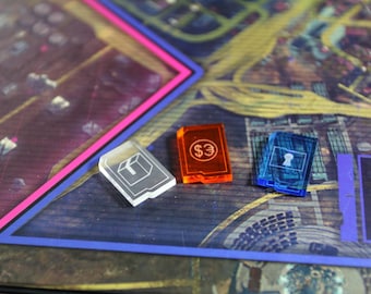 May include: Three game pieces for a board game. The pieces are made of clear plastic and have different symbols on them. One piece is a clear plastic box, one is orange with a dollar sign, and one is blue with a keyhole.