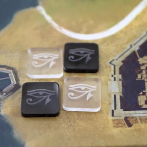 May include: Four game pieces with an eye of Horus design. Two pieces are black with a white eye of Horus design and two pieces are white with a black eye of Horus design.