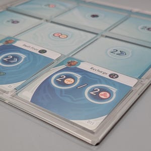 May include: A close-up of a game board with cards featuring different illustrations and text. The cards are labeled with numbers and have a blue and white color scheme. The text on the cards includes "Swift Foot", "Heal 2", "Recharge", and "20/2".