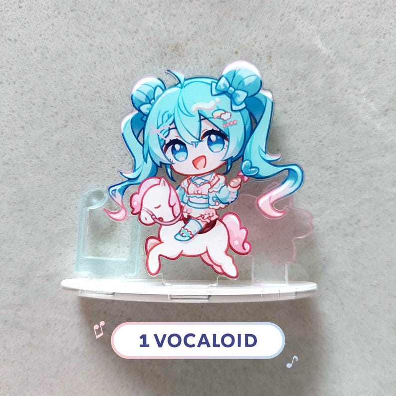 Op de afbeelding: Een acryl display met een chibi-stijl personage met lang blauwgroen haar in staartjes, gekleed in een lichtblauwe en roze outfit, rijdend op een wit paard. Het personage heeft grote blauwe ogen en een glimlach. De tekst 1 VOCALOID is zichtbaar.