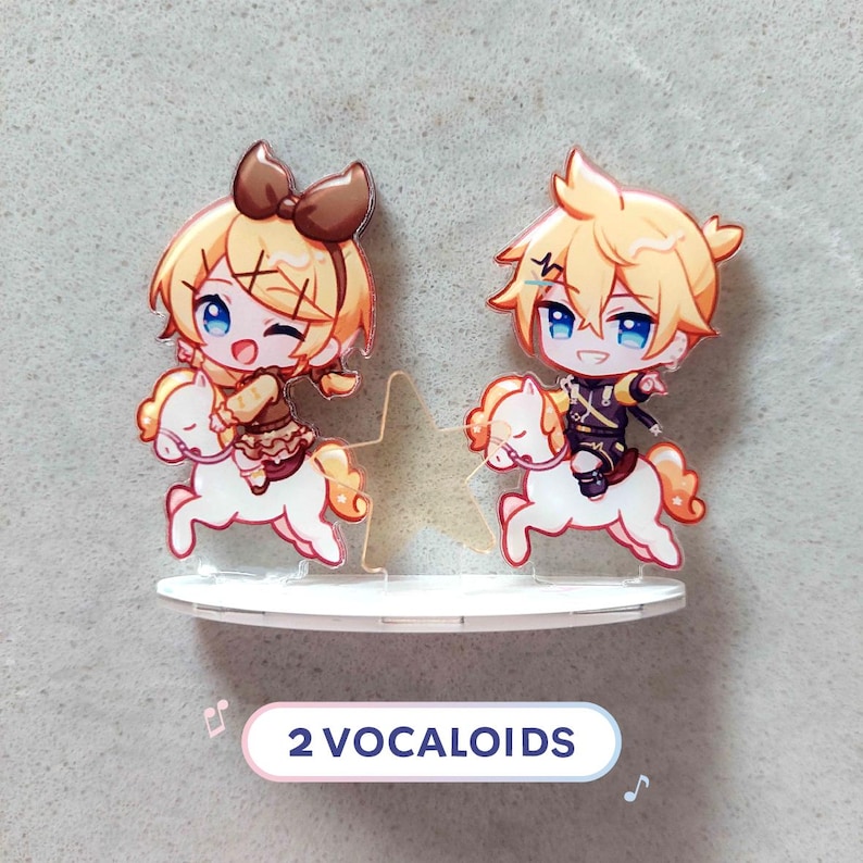 Op de afbeelding: Een acryl display met twee chibi-stijl figuren met blond haar, elk rijdend op een klein wit paard. Tussen de figuren staat een doorzichtige ster. De figuren zijn gemonteerd op een witte voet. De tekst 2 VOCALOIDS is zichtbaar.