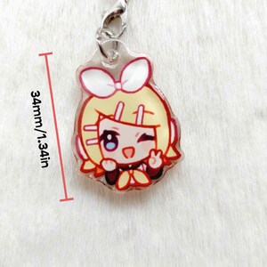 May include: A clear acrylic charm featuring a cartoon character with yellow hair, a white bow, and a red outline. The charm is 1.34 inches (34mm) in height and has a silver clasp.