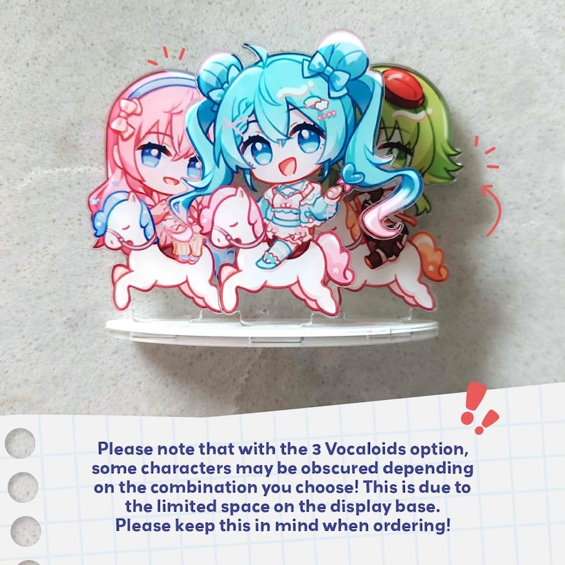 Op de afbeelding: Een acryl displaystandaard met drie chibi-stijl figuren met roze, groenblauw en groen haar, elk rijdend op een wit carrouselpaard. De figuren zijn geplaatst op een ronde witte voet, inclusief een opmerking over de positionering van de figuren.