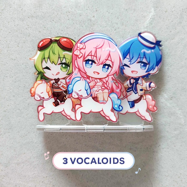 Op de afbeelding: Een acryl display met drie chibi-stijl figuren met groen, roze en blauw haar, elk rijdend op een klein wit paard. De figuren dragen kleurrijke outfits en staan op een doorzichtige voet. Onderaan staat de tekst 3 VOCALOIDS.