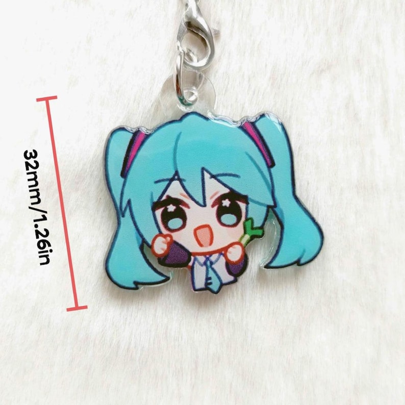 May include: A cartoon charm featuring a character with turquoise hair and pink accents, holding a green object. The charm is 1.26 inches (32mm) in height and is attached to a silver-colored clasp.