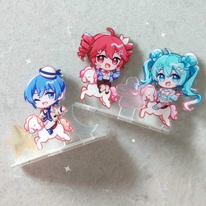 Op de afbeelding: Drie acryl standaards met chibi-stijl personages die op kleine witte paarden rijden. E&eacute;n personage heeft blauw haar en een matrozenmuts, &eacute;&eacute;n heeft roze haar en &eacute;&eacute;n heeft talingkleurig haar. Elke figuur staat op een doorzichtige voet met sterren.