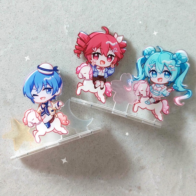 Op de afbeelding: Drie acryl standaards met chibi-stijl personages die op kleine witte paarden rijden. E&eacute;n personage heeft blauw haar en een matrozenmuts, &eacute;&eacute;n heeft roze haar en &eacute;&eacute;n heeft talingkleurig haar. Elke figuur staat op een doorzichtige voet met sterren.