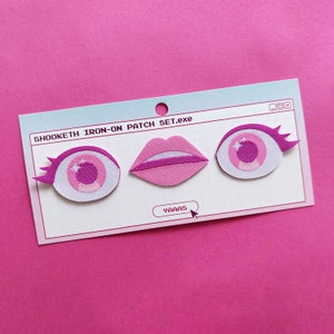 Puede incluir: Un conjunto de tres parches termoadhesivos con ojos rosas con pestañas y labios rosas. Los parches están sobre una tarjeta azul claro con el texto "SHOOKETH IRON-ON PATCH SET.exe" y "YAAAS".