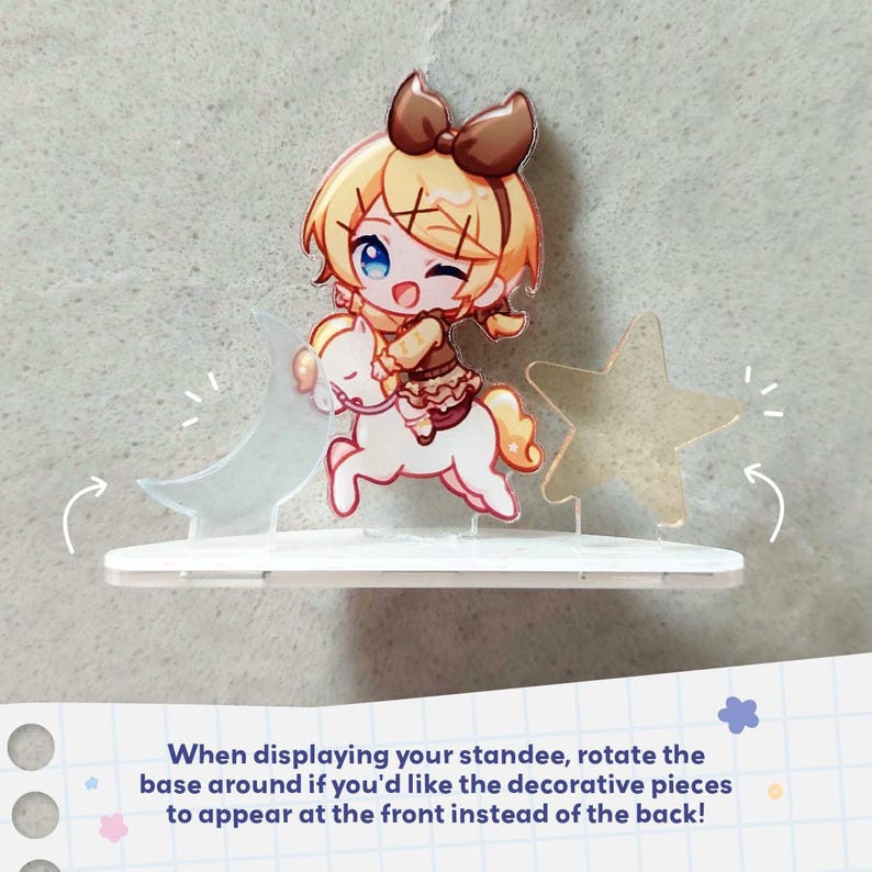 Op de afbeelding: Een acryl display met een blond personage met een bruine strik op een wit paard, geflankeerd door een doorschijnende halve maan en een ster. De voet is wit, met de tekst: When displaying your standee, rotate the base around.