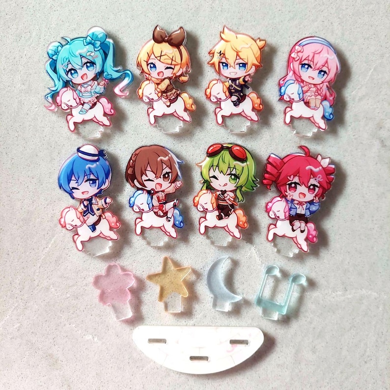 Op de afbeelding: Een verzameling van acht acrylfiguurhangers met anime-stijl personages op kleine witte paarden, vergezeld door vier kleinere doorschijnende hangers in de vorm van een bloem, een ster, een halve maan en een muzieknoot, plus een witte basis.