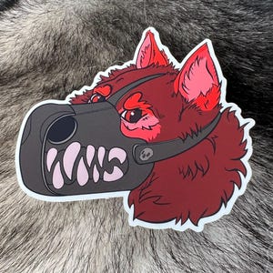 May include: A sticker featuring a stylized red wolf head with a black muzzle and the letters "WWS" in white. The wolf has red eyes and ears, and a skull detail on the muzzle strap. The sticker is on a textured gray background.