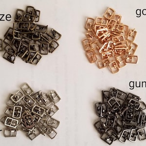 May include: Assortment of metal buckles in four colors: bronze, gold, gunmetal, and silver. Each color is displayed in a separate pile.