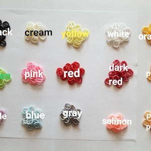 May include: A collection of small, decorative zipper pulls in various colors, including black, cream, yellow, white, orange, green, pink, red, dark red, peach, purple, blue, gray, salmon, and pale peach. Each pull is labeled with its color.