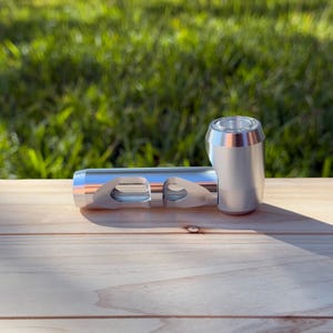 May include: A silver metal smoking pipe with a round bowl and a long, rectangular stem. The stem has two holes on the side.