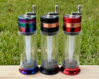 May include: Three glass herb grinders with different colored metal tops. The grinder on the left has a rainbow iridescent top, the middle grinder has a black top with a copper band, and the grinder on the right has a red top with a copper band.