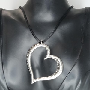 May include: A silver heart-shaped pendant necklace with a black cord. The heart pendant has a textured, hammered finish.