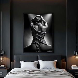 Könnte beinhalten: Ein Schwarzweißfoto einer mit einem Seil gefesselten Person, das an einer Wand in einem dunklen Schlafzimmer mit einem schwarzen Lederbett und Nachttischen hängt.