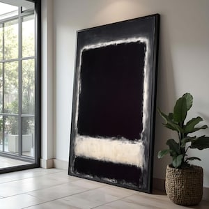 Pode incluir: Grande pintura abstrata emoldurada. A obra apresenta um grande retângulo preto com uma borda branca e uma faixa branca horizontal. A pintura está encostada a uma parede branca, ao lado de uma janela e de uma planta em vaso.