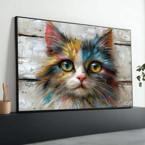 Può includere: Stampa su tela incorniciata di un volto di gatto. Il gatto ha grandi occhi gialli e un naso rosa. La pelliccia è un mix di colori, tra cui blu, giallo, rosa e bianco, con uno stile pittorico e materico. Lo sfondo è in legno bianco invecchiato.