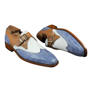 Handmade blue and white spectator monk strap shoes for men featuring premium leather construction, elegant brogue detailing, and artisan craftsmanship.

Two tone monk strap dress shoes crafted from genuine cowhide leather with vintage-inspired formal styling and durable leather sole.

Elegant handmade men’s formal shoes featuring blue leather finish, white contrast panels, monk buckle closure, and handcrafted detailing.