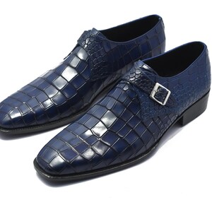 May include: A pair of navy blue leather dress shoes with a square toe and a textured, crocodile-like pattern. Each shoe features a silver buckle closure and a black sole. The shoes are displayed on a white background.