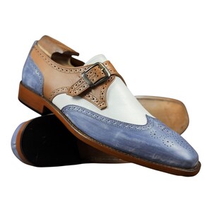 Handmade blue and white spectator monk strap shoes for men featuring premium leather construction, elegant brogue detailing, and artisan craftsmanship.

Two tone monk strap dress shoes crafted from genuine cowhide leather with vintage-inspired formal styling and durable leather sole.

Elegant handmade men’s formal shoes featuring blue leather finish, white contrast panels, monk buckle closure, and handcrafted detailing.
