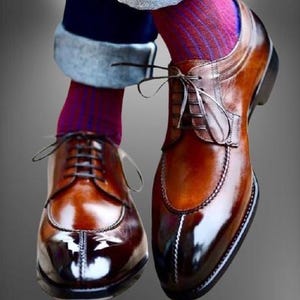 Peut inclure: Une paire de chaussures en cuir marron à lacets avec une pointe pointue et une finition polie. Les chaussures présentent un détail de couture décorative sur la pointe et une semelle noire contrastante.