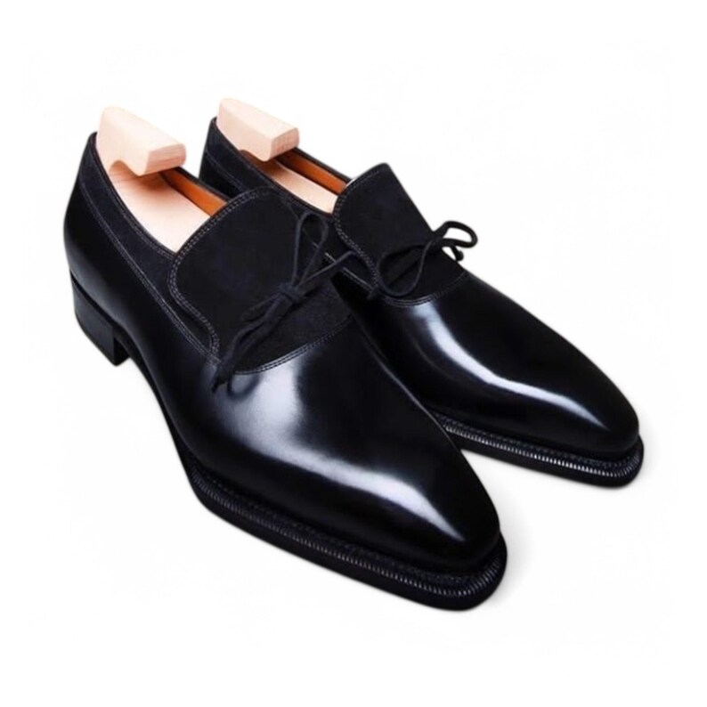 A pair of handmade men's black wholecut derby shoes featuring a polished leather vamp and suede quarters. Elegant formal shoes with a sleek silhouette.