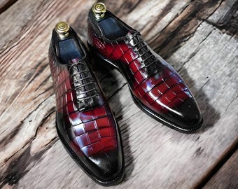 May include: A pair of formal leather shoes with a burgundy and black crocodile-embossed design. The shoes have a lace-up closure and a pointed toe.