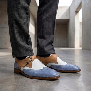 Handmade blue and white spectator monk strap shoes for men featuring premium leather construction, elegant brogue detailing, and artisan craftsmanship.

Two tone monk strap dress shoes crafted from genuine cowhide leather with vintage-inspired formal styling and durable leather sole.

Elegant handmade men’s formal shoes featuring blue leather finish, white contrast panels, monk buckle closure, and handcrafted detailing.