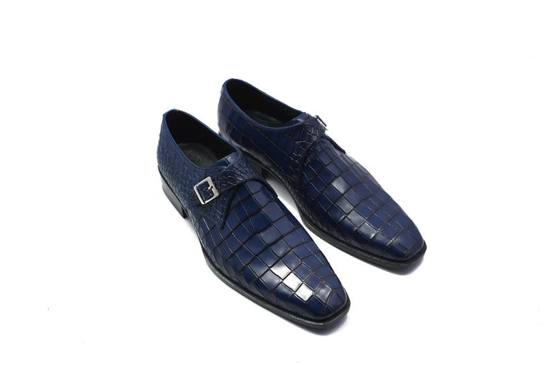 May include: A pair of navy blue leather dress shoes with a square, textured pattern. Each shoe features a silver buckle closure. The shoes are set against a white background.