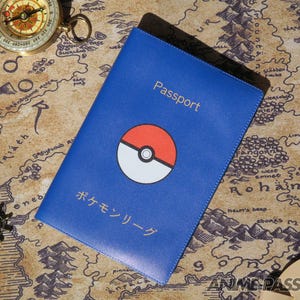 May include: Blue passport holder with gold lettering reading "Passport". It features a red, white, and black graphic. Japanese text is also visible. The passport holder is on a map.