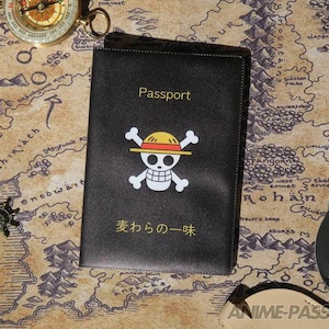 May include: Black passport cover with the word "Passport" in gold lettering. Features a white skull and crossbones logo with a yellow and red straw hat. Japanese text is below the logo. The passport is on a map.