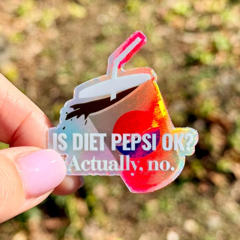 May include: A holographic sticker shaped like a soda cup with a straw, featuring a red and blue circular logo. The text reads IS DIET PEPSI OK? Actually, no. The sticker has a reflective, iridescent finish that shifts colors when viewed from different angles.