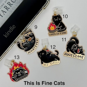 May include: A collection of black cat charms with gold accents, each featuring a different expression and phrase. Phrases include "Whatever," "This is Fine," "Awesome," and "Treat Yourself." The charms are attached to clear phone accessories.
