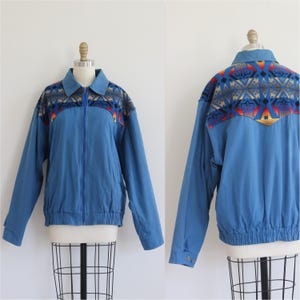 Peut inclure: Une veste zippée bleue dotée d'un col pointu et d'un motif géométrique multicolore vif sur le haut de la poitrine et le dos. La veste comprend des manches longues avec des poignets boutonnés et une taille élastiquée à l'ourlet inférieur.