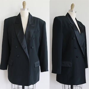 May include: A black double-breasted blazer with a satin lapel and two rows of buttons. The blazer has two front pockets and is displayed on a mannequin. The jacket has a classic, tailored design.