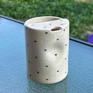 Peut inclure: Une tasse en c&eacute;ramique blanche avec une anse noire et le texte "But First, Coffee" en noir, dans une police manuscrite. La tasse est pos&eacute;e sur une surface blanche.