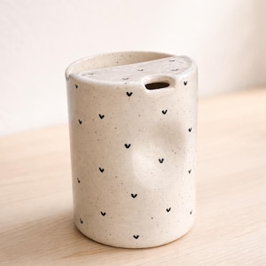 Peut inclure: Une tasse en c&eacute;ramique blanche avec une anse noire et l'inscription "But First, Coffee" en gras noir. La tasse est pos&eacute;e sur un fond flou, sugg&eacute;rant un cadre chaleureux.